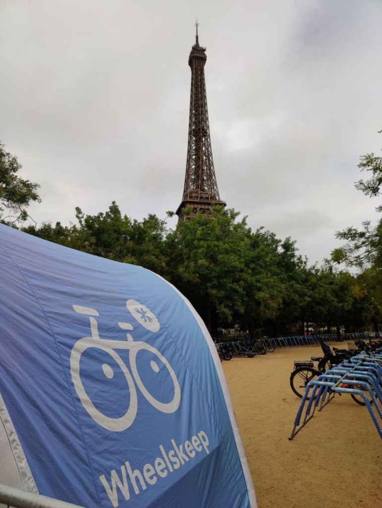 Blue banner with a white bicycle graphic and the word 'Wheelskep' in a bike parking area, with the Eiffel Tower visible in the background.